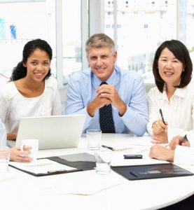 three people smiling and sitting around desk